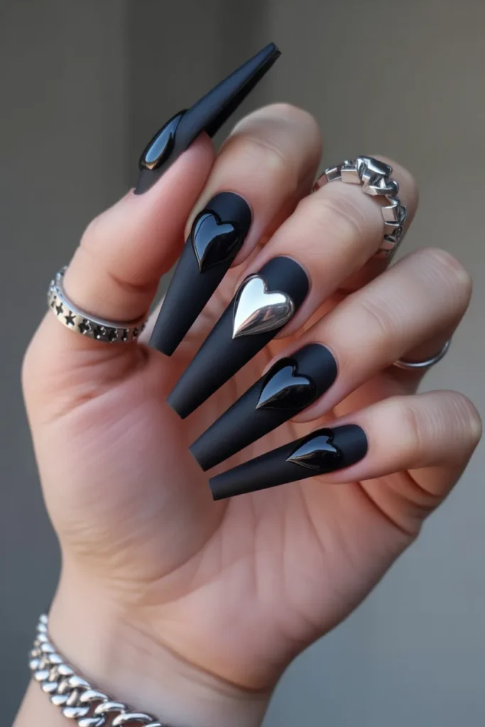 Long coffin nails with matte black base, glossy black hearts and silver chrome heart accents, moody dramatic lighting with silver jewelry, modern gothic Valentine’s nail design.